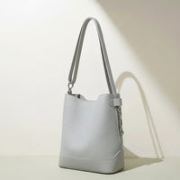Minimalist light grey leather bucket bag with shoulder strap on neutral background