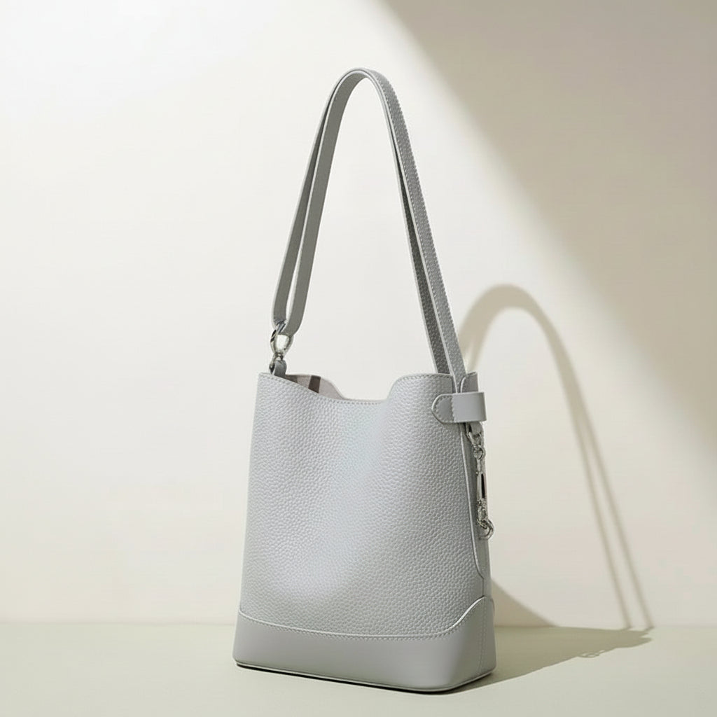 Minimalist light grey leather bucket bag with shoulder strap on neutral background
