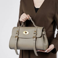 Woman in brown blazer holding taupe leather handbag with gold hardware and braided handle