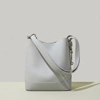 Light grey leather bucket bag with wide strap on neutral background