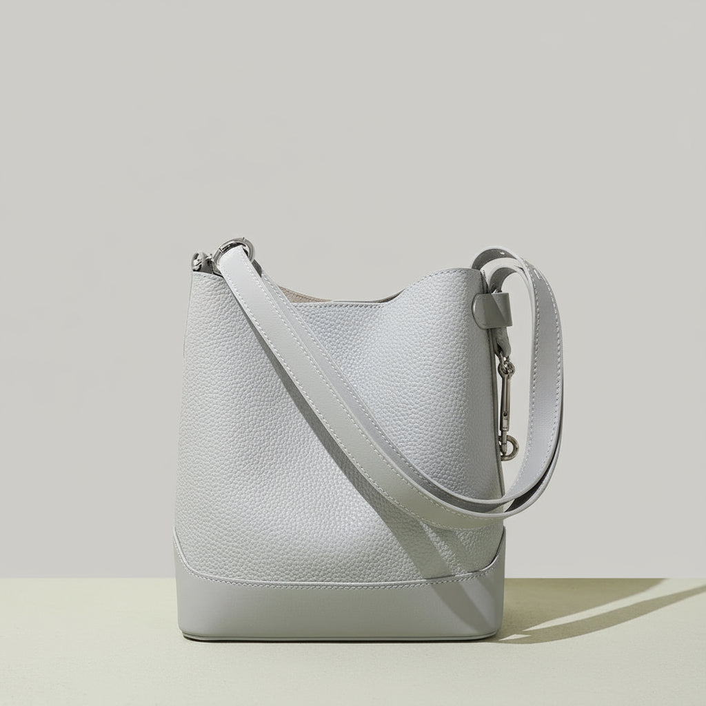 Light grey leather bucket bag with wide strap on neutral background