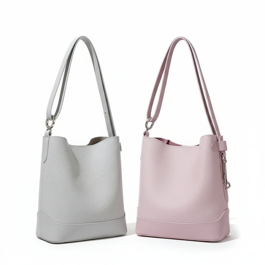 Light grey and pastel pink leather bucket bags with long straps on a neutral background