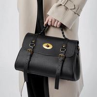 Woman in beige coat holding black leather handbag with gold buckle and braided handle