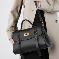 Woman in beige coat holding black leather satchel handbag with gold hardware