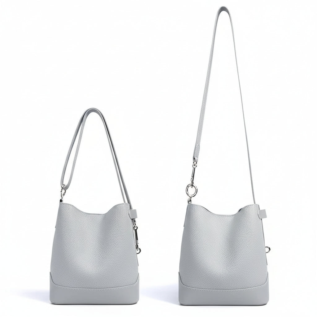 Light gray leather bucket bag with two adjustable shoulder straps on white background