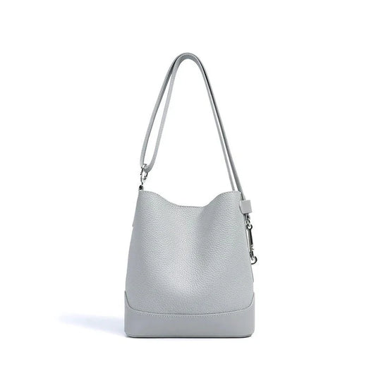 Light grey leather bucket bag with long shoulder strap on white background