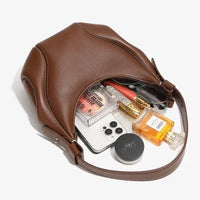 Brown leather handbag with makeup, perfume, sunglasses, and smartphone on white background