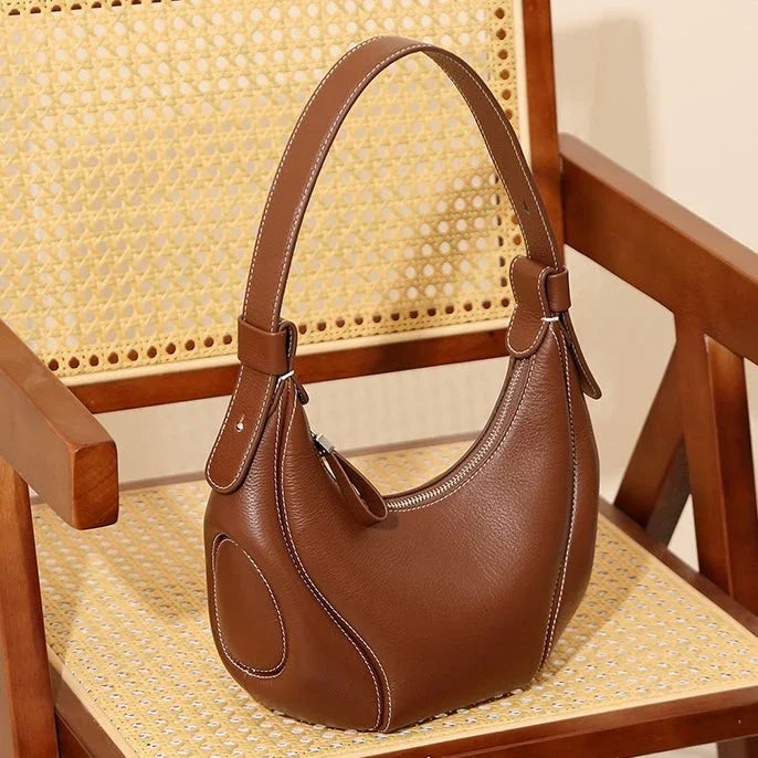 Brown leather handbag with white stitching on a wooden cane chair