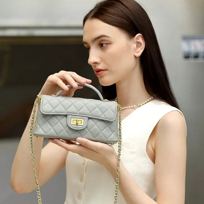 Woman holding quilted gray leather handbag with gold chain strap
