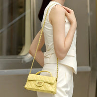 Woman wearing a sleeveless white suit with a small yellow quilted shoulder bag