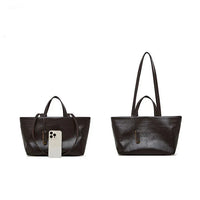 Two black leather tote bags with handles, one shown with a smartphone for size comparison