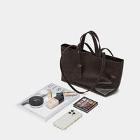 Black leather tote bag with cosmetics, iPhone, magazine, and makeup palette on white background
