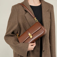 Woman wearing brown herringbone blazer with brown leather shoulder bag and gold clasp