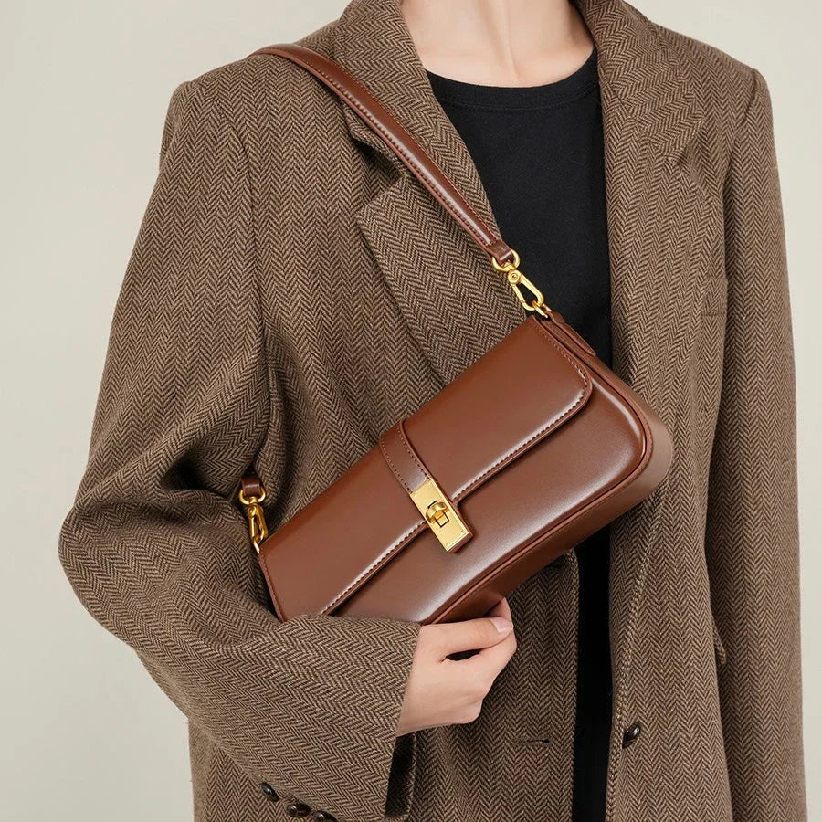 Woman wearing brown herringbone blazer with brown leather shoulder bag and gold clasp