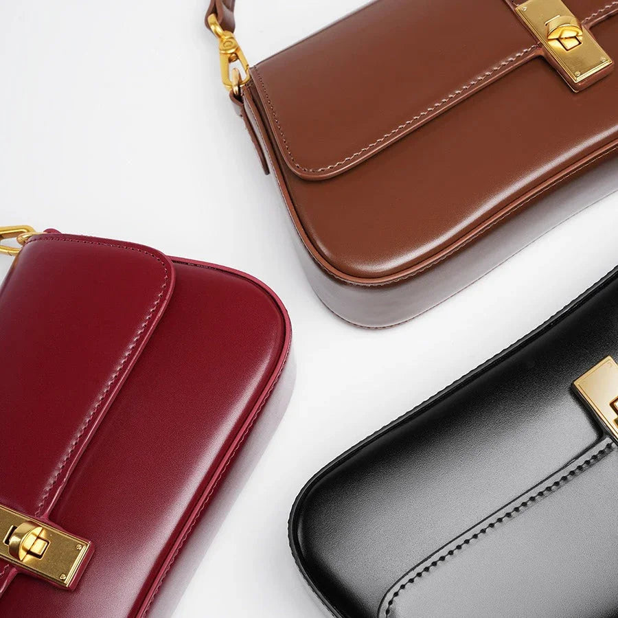 Three leather shoulder bags in brown, red, and black with gold clasps on a white background.