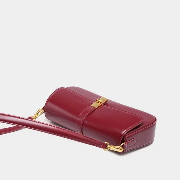 Burgundy leather crossbody bag with gold hardware and adjustable strap on white background