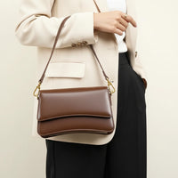 Woman holding brown leather handbag with gold hardware, wearing a herringbone blazer
