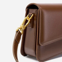 Brown leather shoulder bag with gold hardware and detachable strap on white background