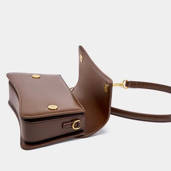 Brown leather crossbody bag with gold hardware and open flap on white background