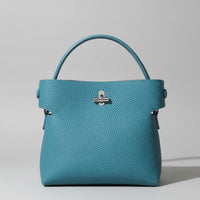 Blue pebbled leather handbag with top handle and silver clasp on light background