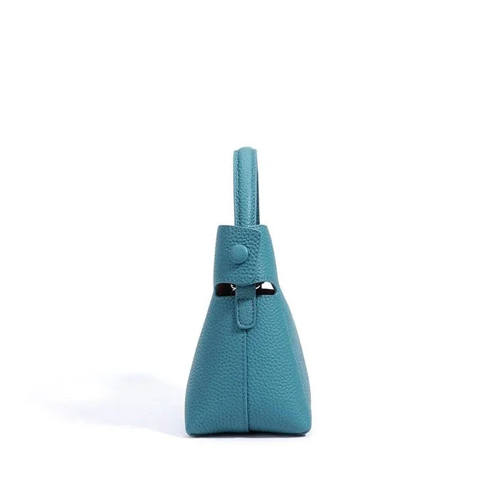 Side view of teal leather handbag with handle on white background