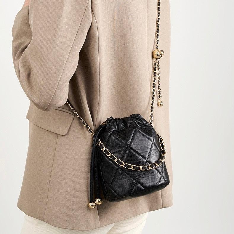 Woman wearing beige blazer with black quilted leather crossbody bag and gold chain strap