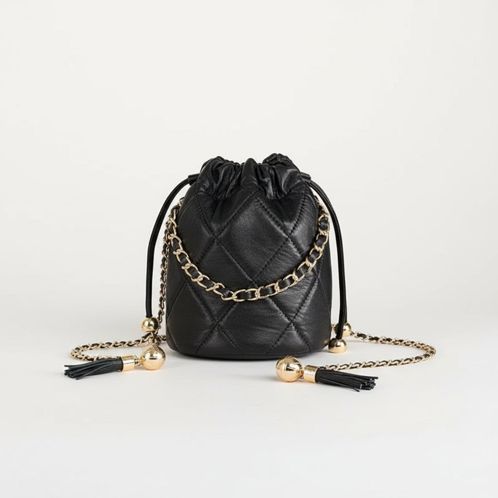Black quilted drawstring purse with gold chain, held by hand against white background