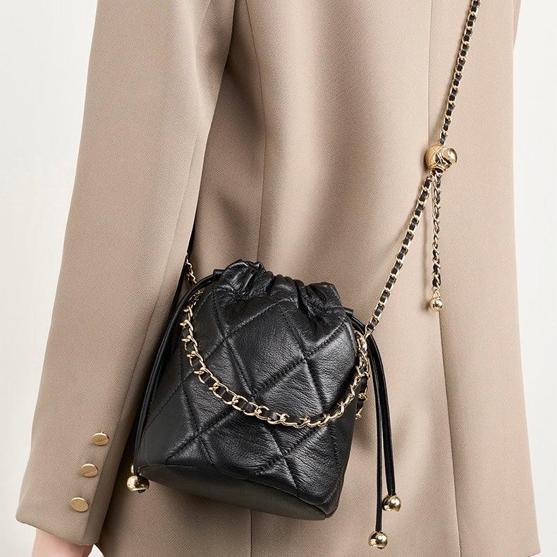 Woman wearing a beige blazer with a black quilted leather bucket bag with gold chain strap