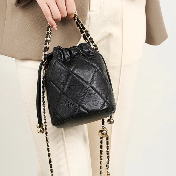Quilted black leather bucket bag with gold chain strap, held by woman in beige outfit
