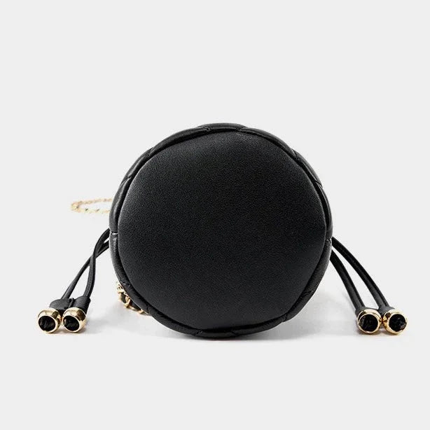 Round black leather crossbody bag with gold accents and side tassels on white background