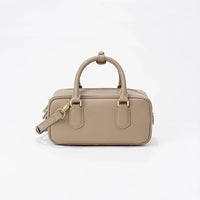 Beige leather handbag with gold hardware and top handle on white background