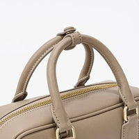 Beige leather handbag with gold zipper and double handles on white background