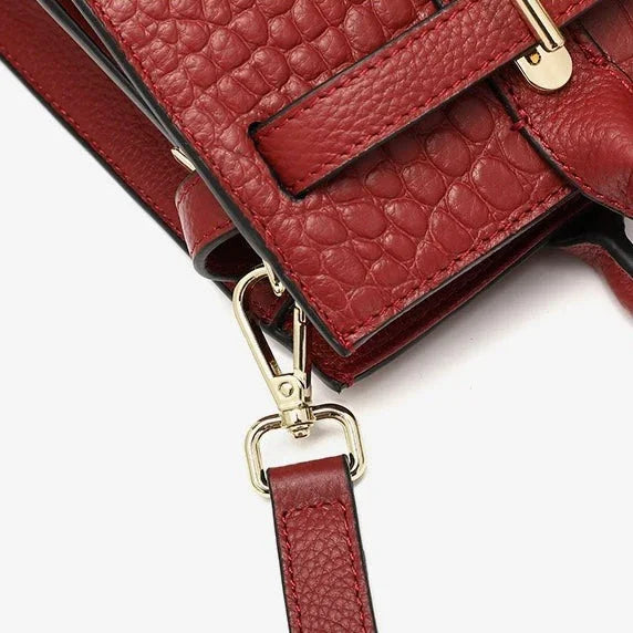 Close-up of red textured leather handbag with gold hardware and detachable strap