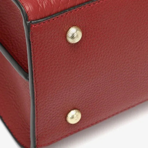 Close-up of red leather handbag corner with gold metal feet and black trim