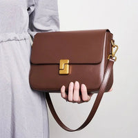 Woman holding a brown leather crossbody bag with gold clasp and adjustable strap