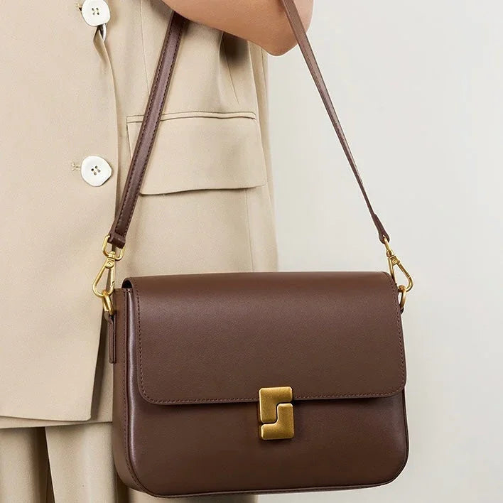 Brown leather shoulder bag with gold clasp, worn over beige blazer