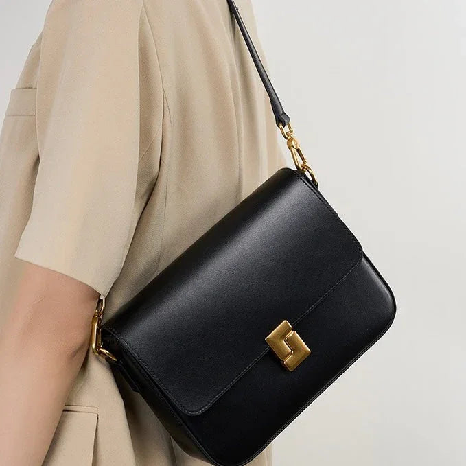 Black leather shoulder bag with gold clasp worn over a beige short-sleeve outfit