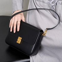 Woman holding a black leather shoulder bag with gold clasp, stylish accessory