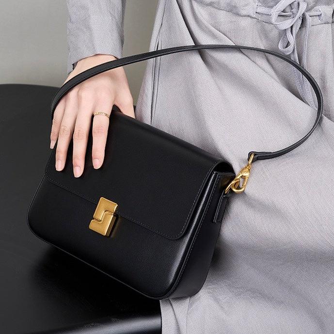 Woman holding a black leather shoulder bag with gold clasp, stylish accessory