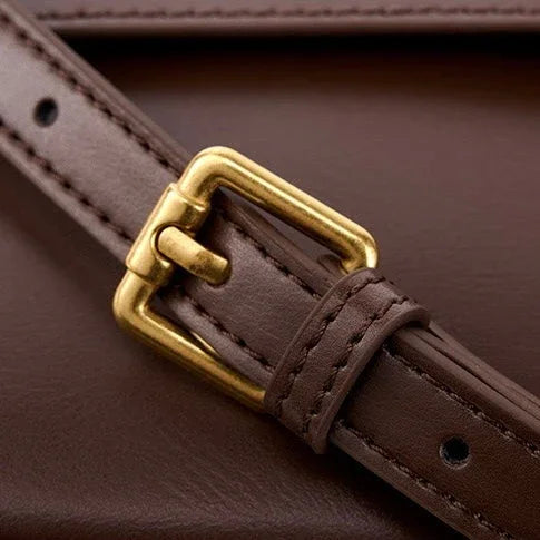 Brown leather strap with gold buckle on brown leather surface