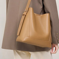 Tan leather bucket bag with adjustable strap worn on shoulder over taupe blazer