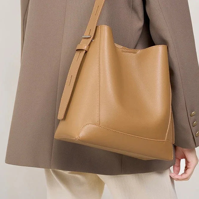 Tan leather bucket bag with adjustable strap worn on shoulder over taupe blazer