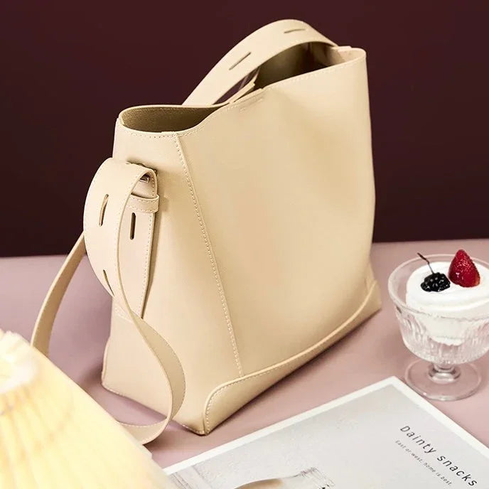 Beige leather tote bag on pink table with dessert and magazine