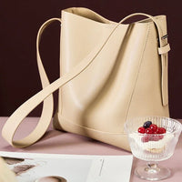 Beige leather bucket bag on table with fruit parfait and magazine, minimalist style