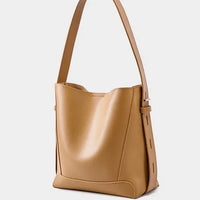 Tan leather bucket bag with wide shoulder strap on white background