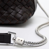 Close-up of woven dark leather bag with silver chain strap on white background