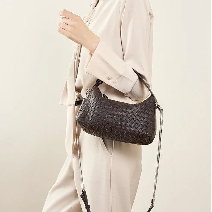 Woman in beige outfit holding a black woven leather shoulder bag with chain strap