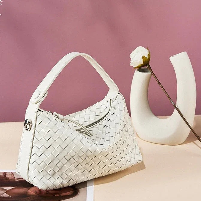 White woven handbag on beige table with modern vase and rose, pink background
