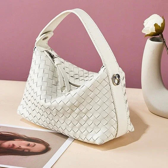 White woven leather handbag on beige table, pink background, next to vase with white flower