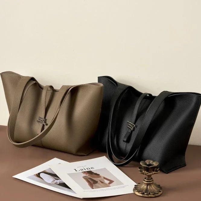 Taupe and black leather tote bags on table with magazines and brass candle holder